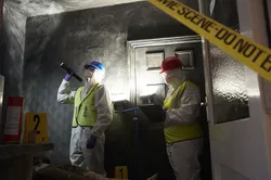Two forensics students in hazmat suits and high vis jackets inspecting a room in the Crime Scene House