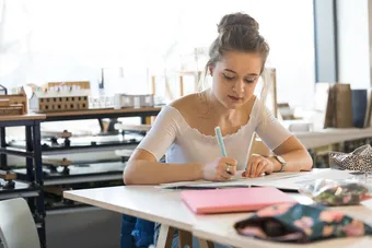 A student working in the interior design facilities with 3D models of buildings in the background.