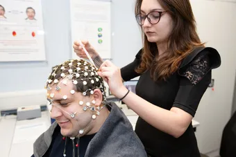 A student applies an EEG to another student's scalp to measure the electrical activity in their brain in a psychology laboratory