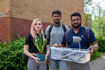 three students with moving boxes and a plant ready to move into student accommodation