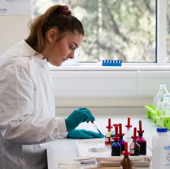 A student in a lab coat and gloves uses a pipette in a science experiement.