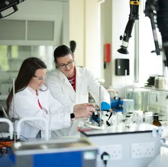 Two students in laboratory coats and blue gloves conduct an experiment in a USW chemistry laboratory