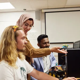 A lecturer talks to two postgraduate students while they all look at a computer with a small electronic car