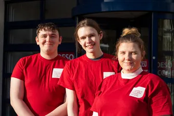 Three student ambassadors are stood with eachother, smiling, and wearing red USW tshirts.
