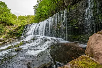 A waterfall surrounded by moss, trees, and stones in Ystradfellte, Neath