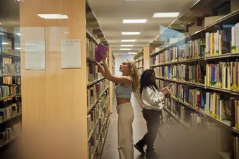 Two students picking out books from a bookshelf in the library.