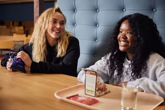 Two students sat in stilts smiling over food