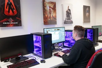 computing student working at computer, with images of video games on the wall above