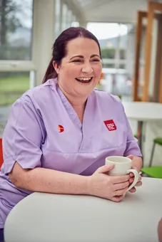 A nurse is sat laughing while enjoying a cup of tea.