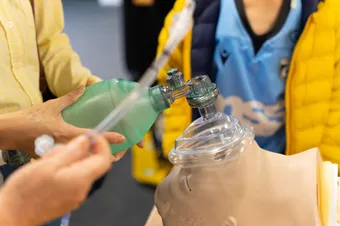 An academic in scrubs is giving an oxygen supply demonstration to a student.