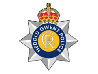 The Gwent Police logo - a crest in the style of a silver police star with the crown of King Charles third on top. In the middle is a yellow circle containing the seal of King Charles surrounded by a navy blue banner saying 