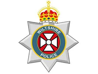 The Wiltshire Police logo - a silver police star crest with the crown of King Charles on top. In the centre is a white cross made up of triangles and a circle in a red circle. A navy blue banner around the outside with gold lining contains the words 