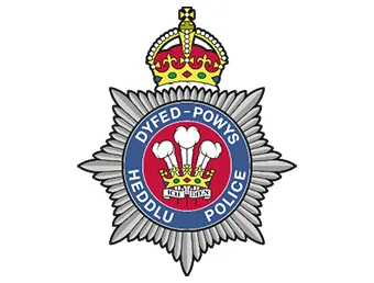 The Heddlu Dyfed-Powys Police logo - a silver police star style crest with the Welsh feathers in the middle in a red circle and their German motto 