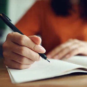A close up of a hand holding a pen, about to begin writing in a notebook