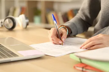 Close up of a person filling out form document sitting on a desk at home