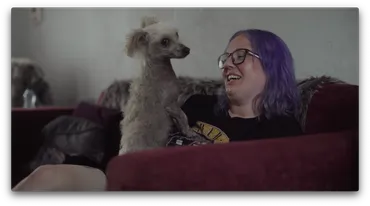 A person is sat on a sofa, smiling, with a dog on their lap.