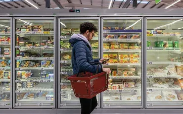 A person shopping in a supermarket and reading the packet of something from the freezer.