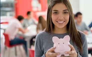 A girl is smiling and holding a pink piggy bank.