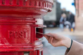 letter being posted into a red post box