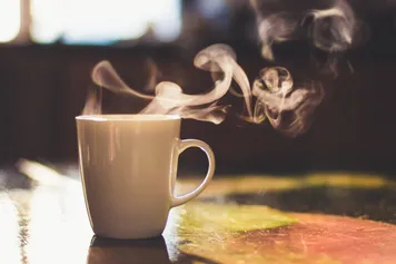 A close up of a steaming cup of tea on a table.