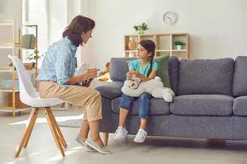 psychologist working with a preschool child in a bright office. Woman makes notes about the condition of the girl on paper