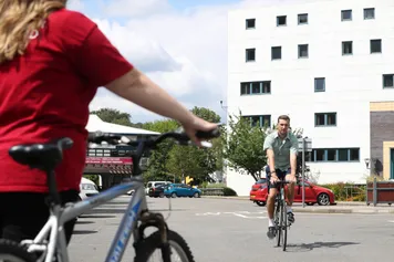 Two students cycling with campus building in the background