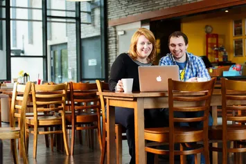 USW student and his mum are sitting together at a table in the Students' Union cafe and looking at a laptop.