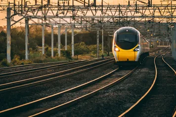 A train travelling along train tracks with the sun setting in the background.