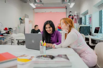 Two students working in a studio space on a laptop.