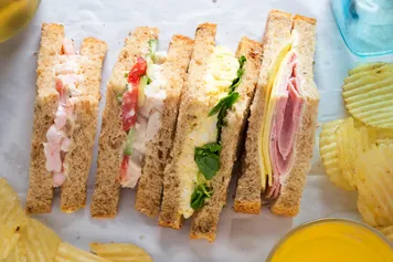 Selection of sandwiches on malted brown bread with crinkle cut crisps. Prawns with mayonnaise. Roast chicken breast, vine tomatoes, cucumber, mayonnaise. Egg mayonnaise and watercress. Ham and cheddar cheese on mayo.