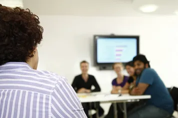 A member of staff talks to their colleagues inside a white USW meeting room with a TV for presenting in the background