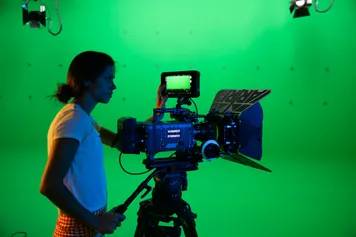 A student using a film camera in front of a green screen.