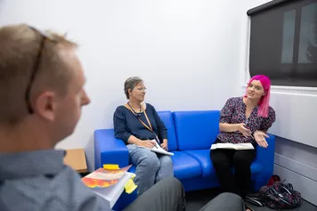 An over the shoulder image of a man talking to two women who are sat on a sofa in a counselling room.