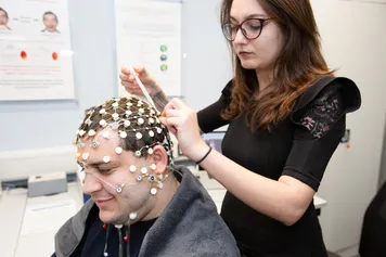 A student applies an EEG to another student's scalp to measure the electrical activity in their brain in a psychology laboratory