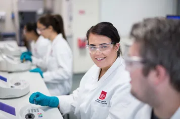 Students wearing lab coats and protective eyewear are working in a forensics lab.