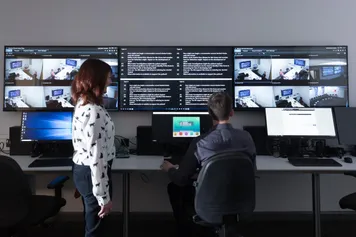 Two academics observing students on the screens in the hydra suite