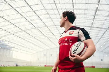 Rugby student stood in Sport Park facilities with pitch behind him