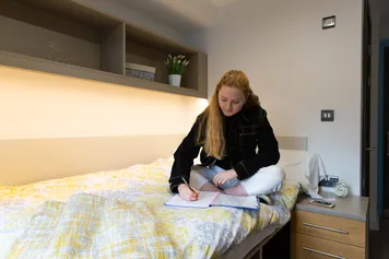 A student sat on a bed writing notes in the Glamorgan Court accommodation.