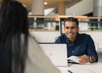 Two MBA Global students working opposite each other on a table in a library setting.