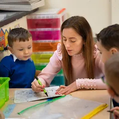 Student on work placement at a primary school using a whiteboard with two pupils sat either side of a table