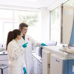 Two forensics students wearing USW laboratory coats and blue science gloves use equipment in a USW laboratory