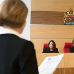 A smartly-dressed student talks to a fellow student sat at the bench in the moot courtroom
