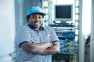 Computer Science Student, Gbren Okmal, smiling for camera standing in front of a computer