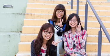 three students sitting on outdoor steps smiling to camera