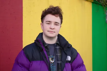 A profile of law student, Ash Taylor, stood against a red, yellow and green painted wall.