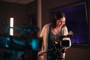 A performance student stands confidently in front of a camera in a studio, ready for filming.