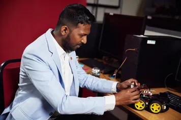 Student Noel Anthony sitting in front of a computer whilst working on a model car