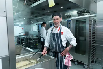 Catering staff, wearing chef whites and an apron, in the University kitchen frying a basket of chips