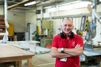 a member of estates and facilities University staff standing in workshop smiling to camera