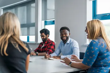 four members of university staff working and having a conversation, smiling